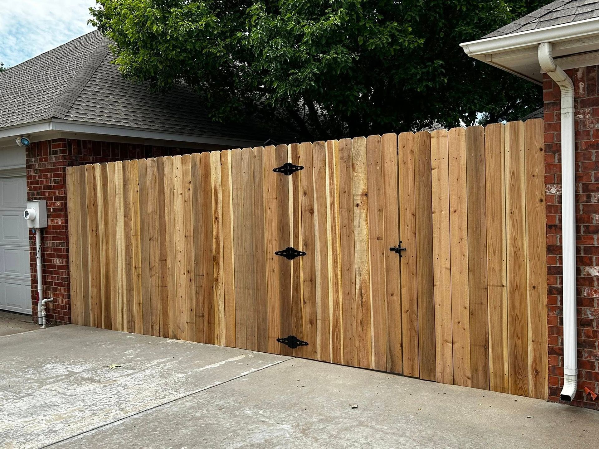 Wooden fence with black hinges, next to brick wall and garage.