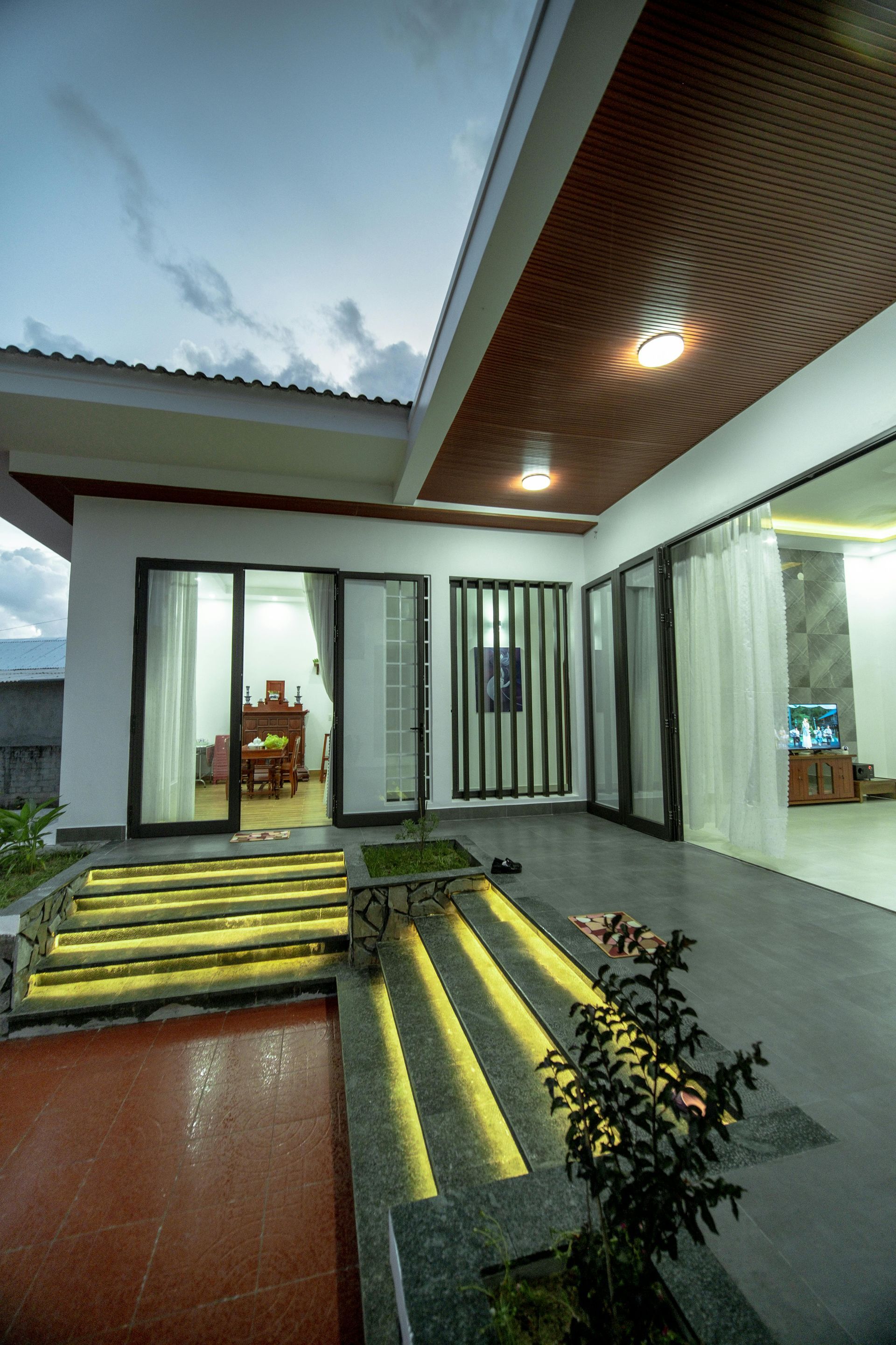 Exterior view of a modern home with illuminated steps, glass doors, and a covered patio.