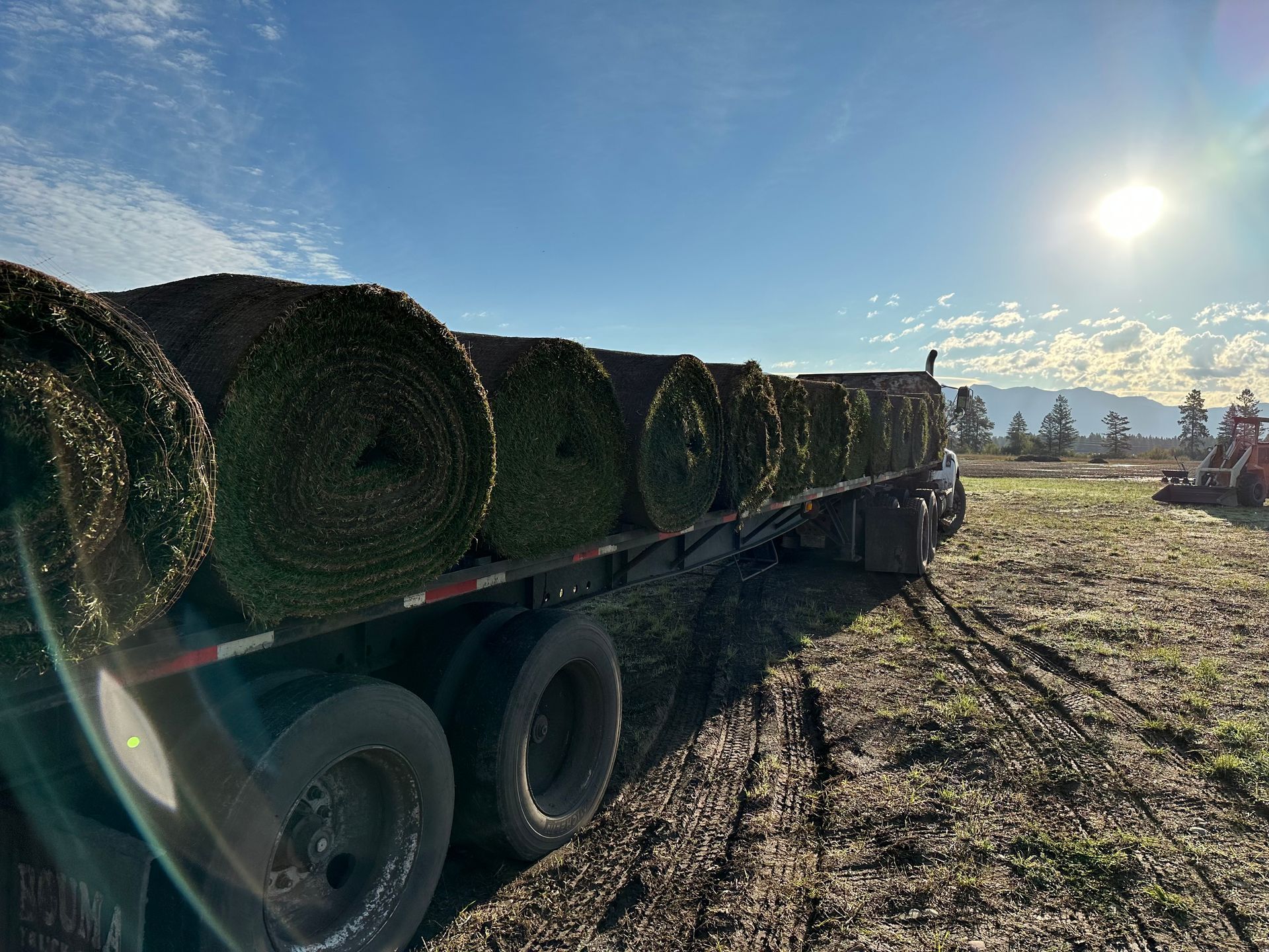 A truck is carrying rolls of grass on a trailer.