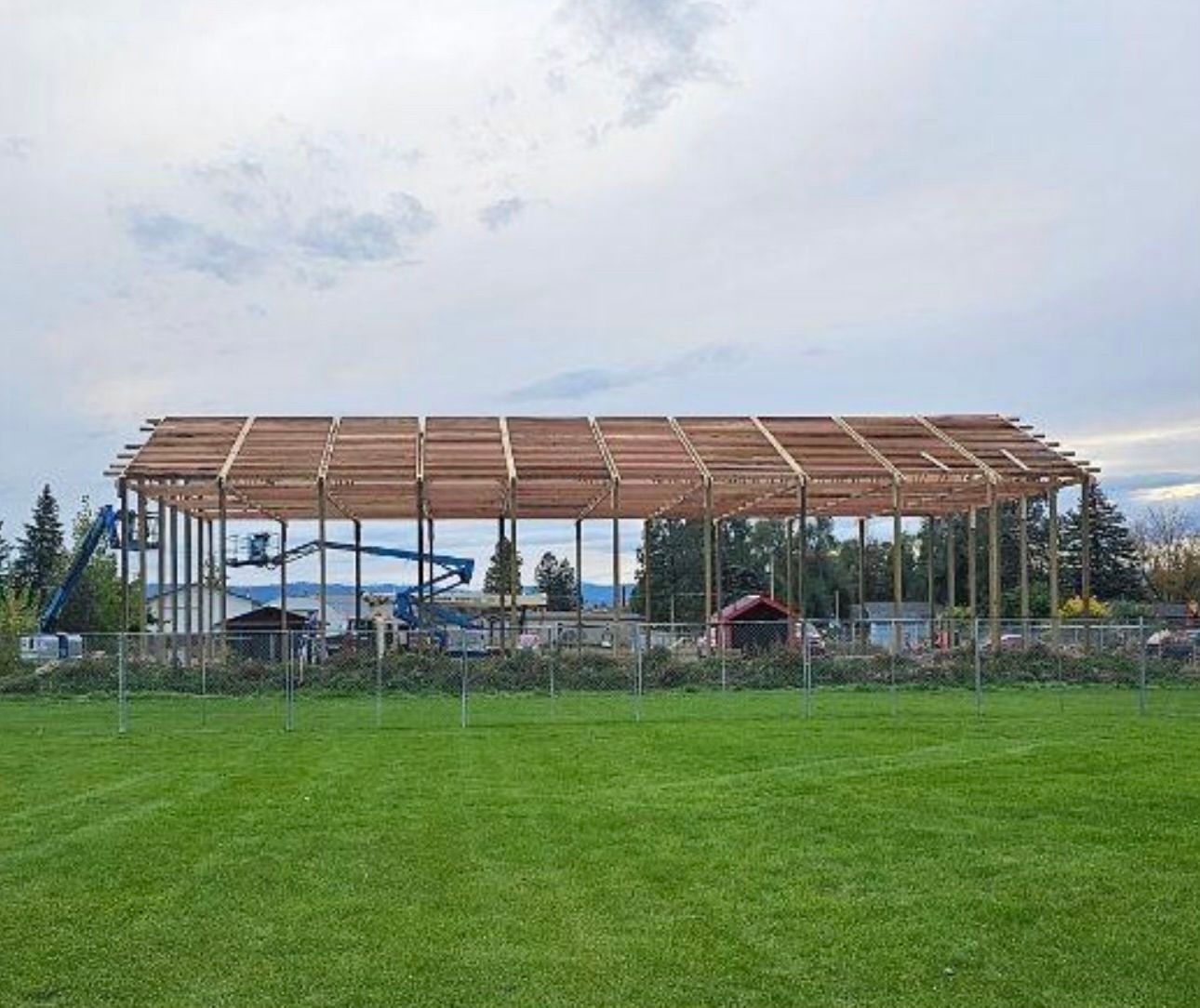 A large wooden structure is being built in a grassy field.