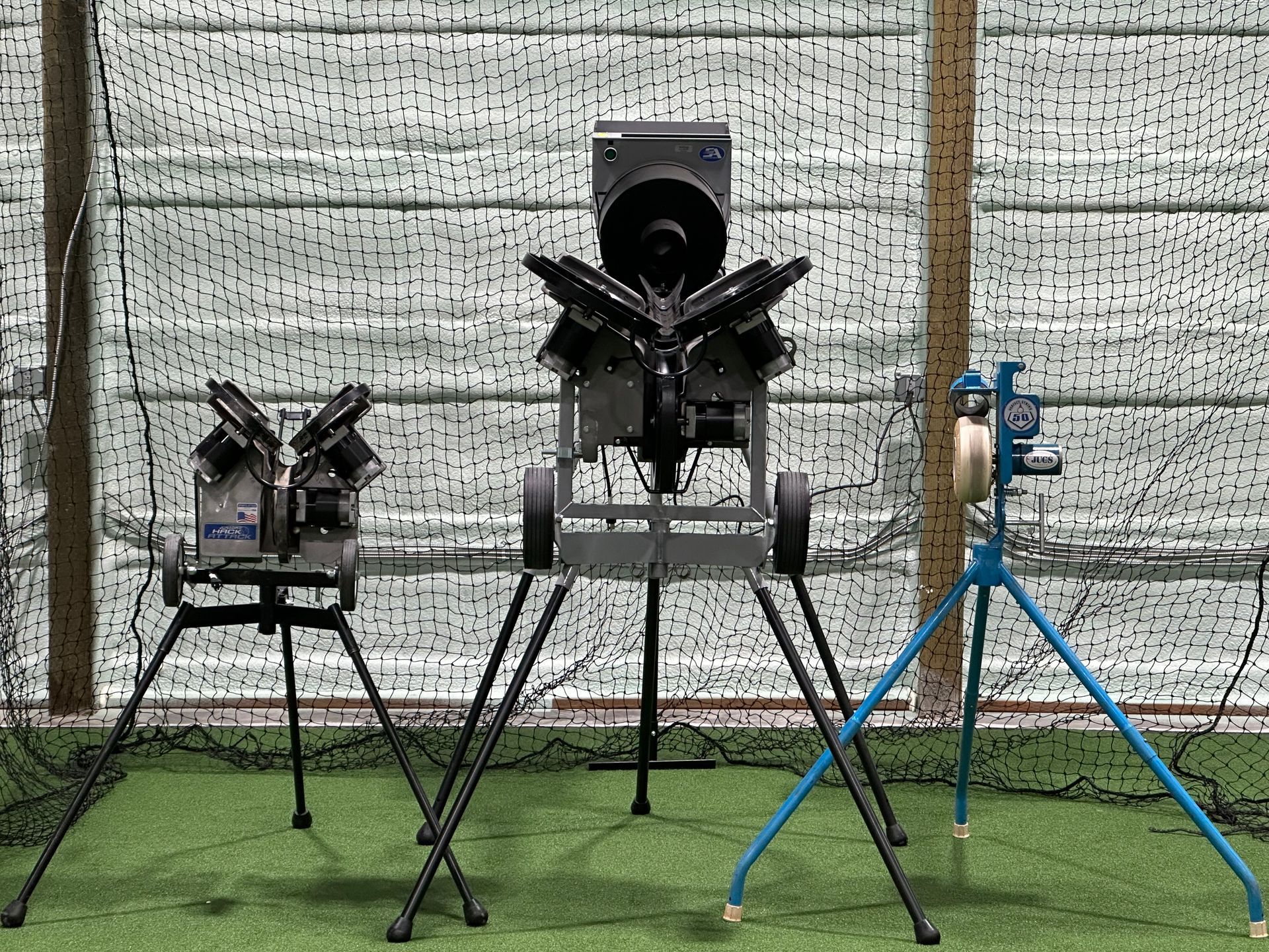 Three baseball pitching machines are sitting on top of a lush green field.