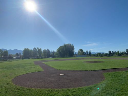 A baseball field with the sun shining through the trees