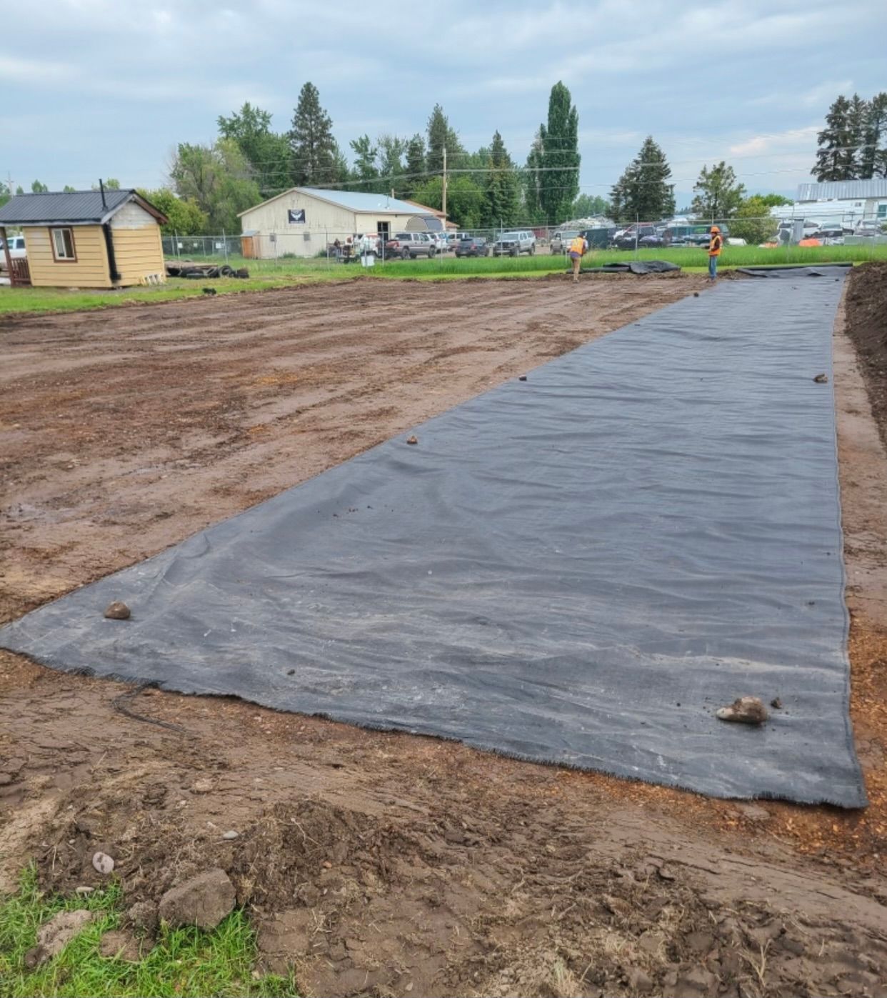 A large black tarp is covering a dirt field.