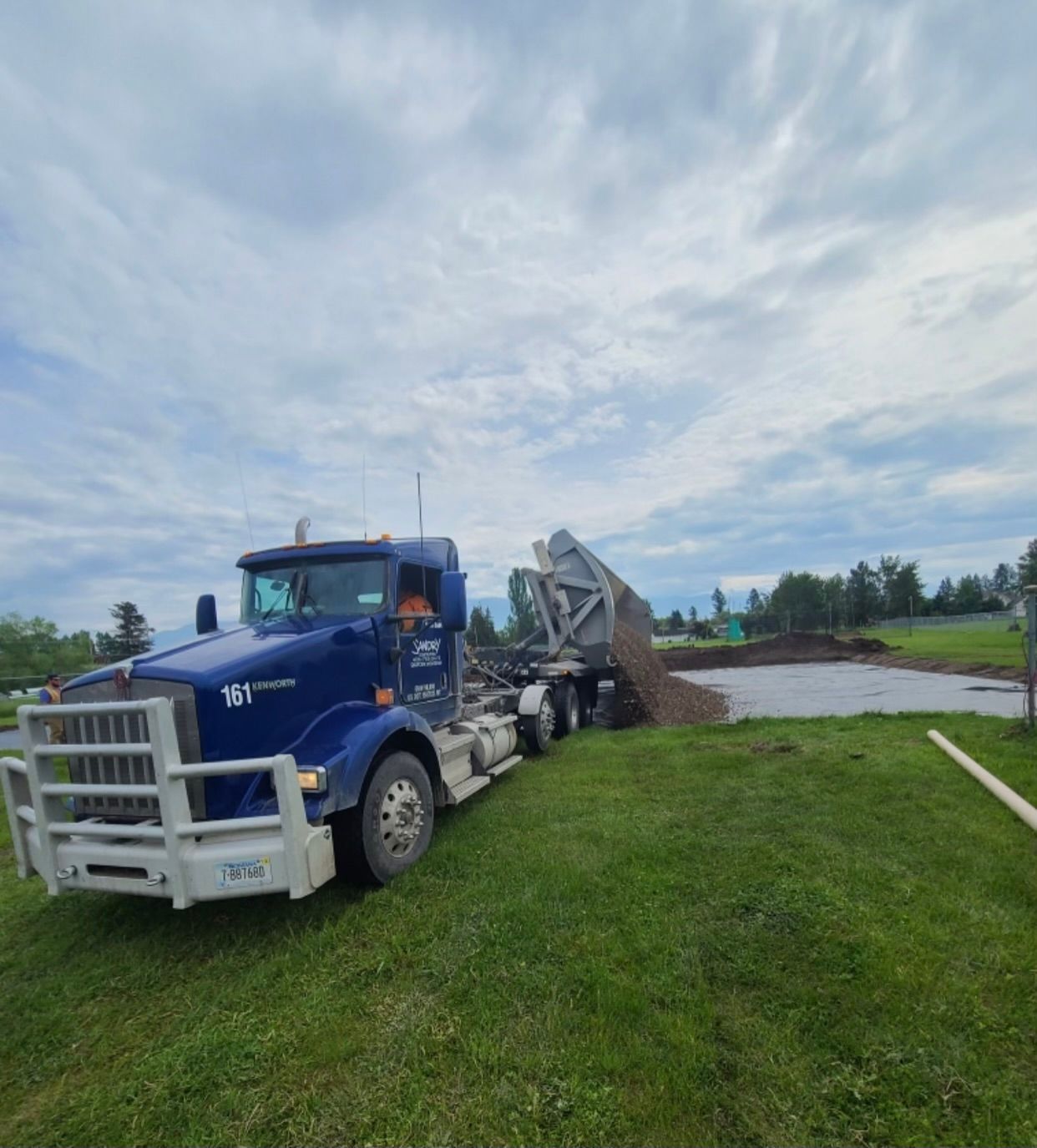 A blue dump truck is parked in a grassy field.