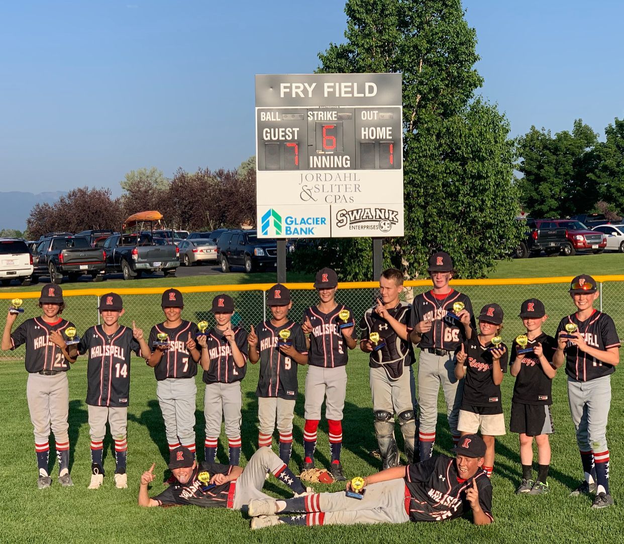 A group of young baseball players are posing for a picture in front of a scoreboard.