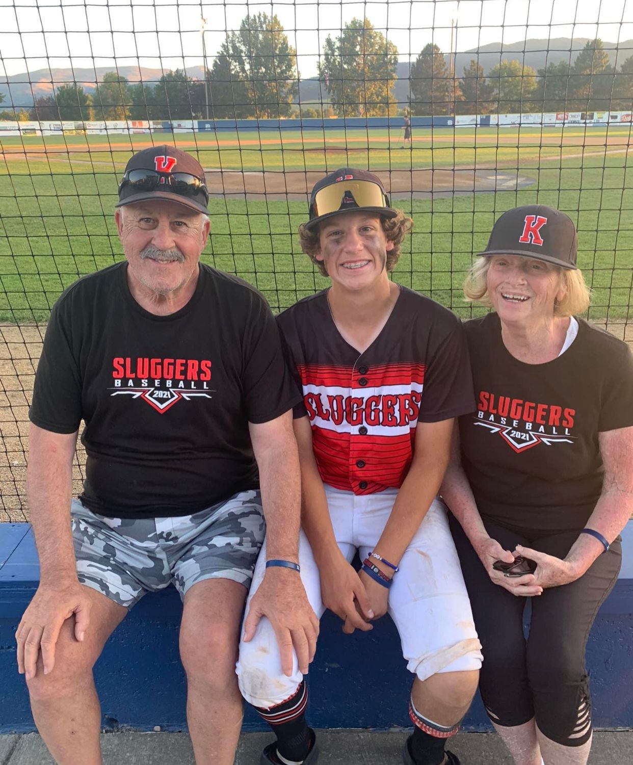 A man and woman are sitting next to a boy wearing a sluggers shirt