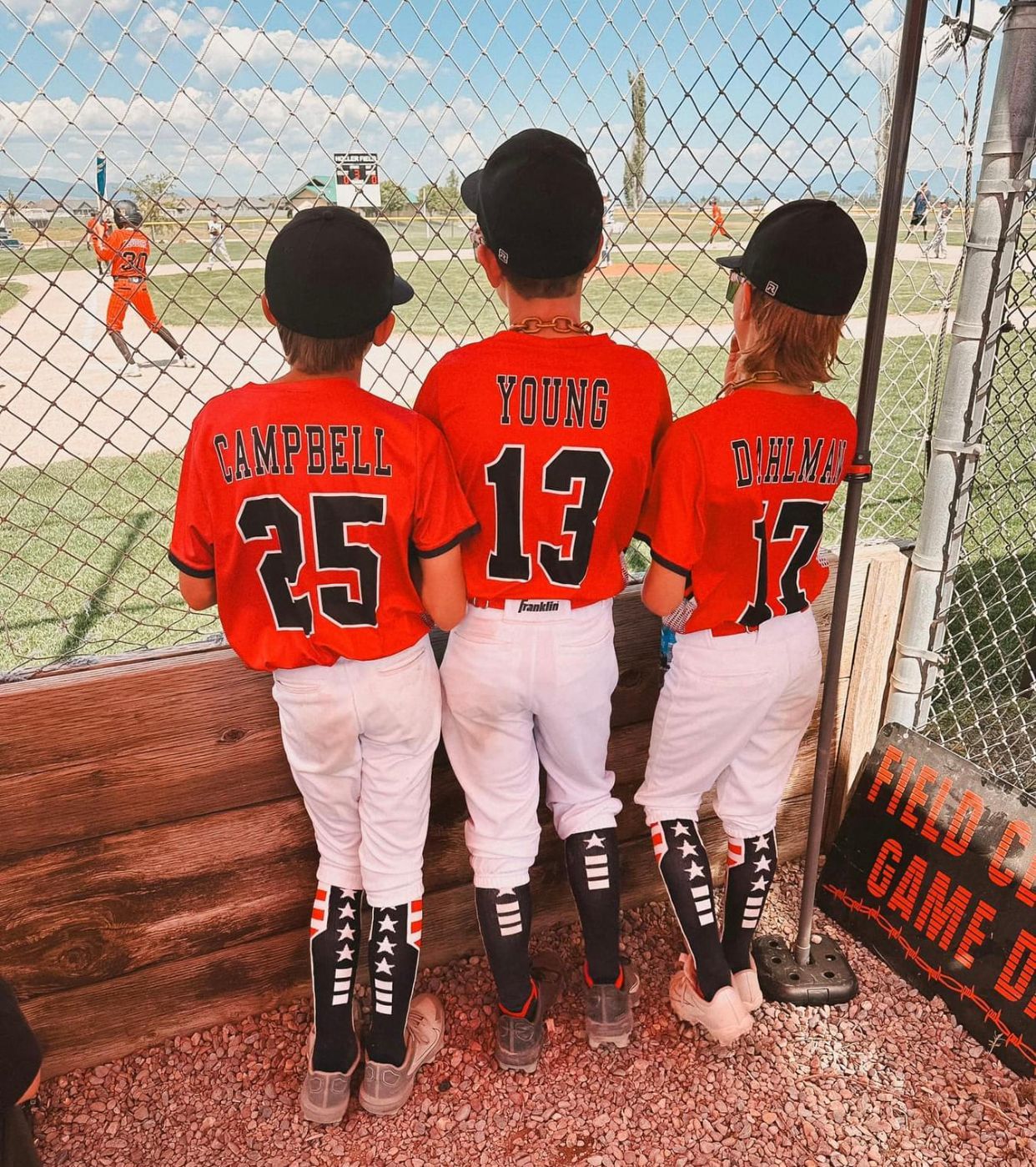 Three young boys in baseball uniforms are standing next to each other on a baseball field.