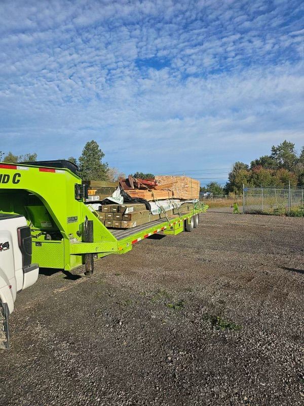 A green trailer is parked in a gravel lot next to a truck.