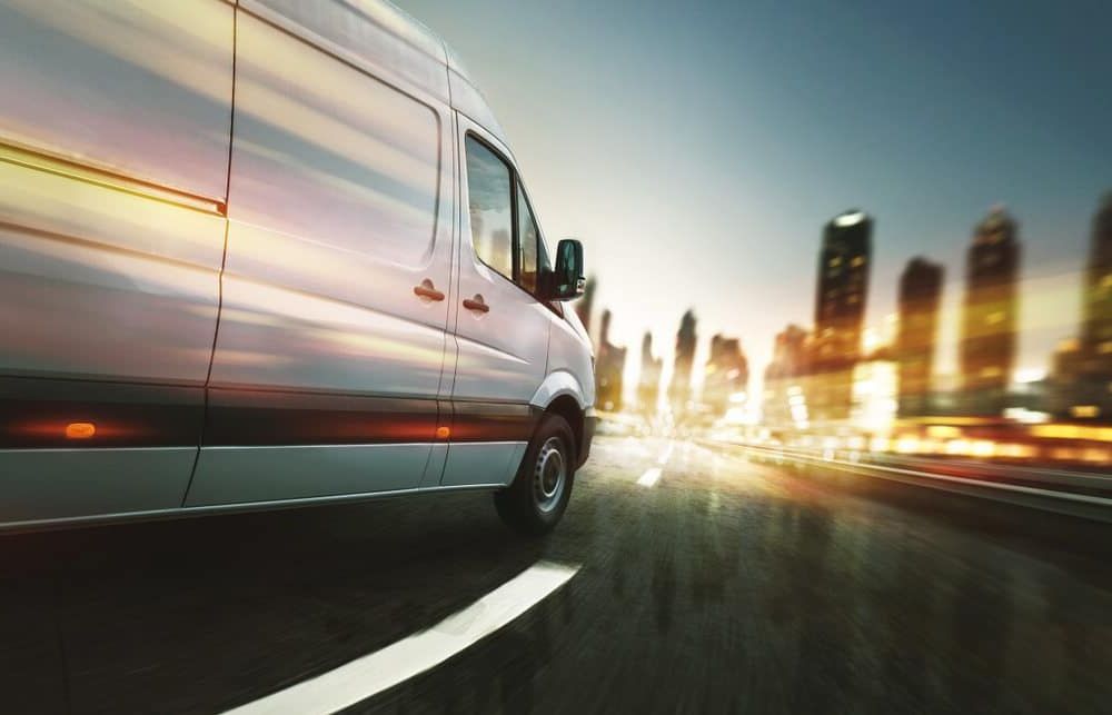 A Delivery Van is Driving Down a Highway in Front of a City Skyline — Regina's Cleaning Group Pty Ltd In Lee Point, NT
