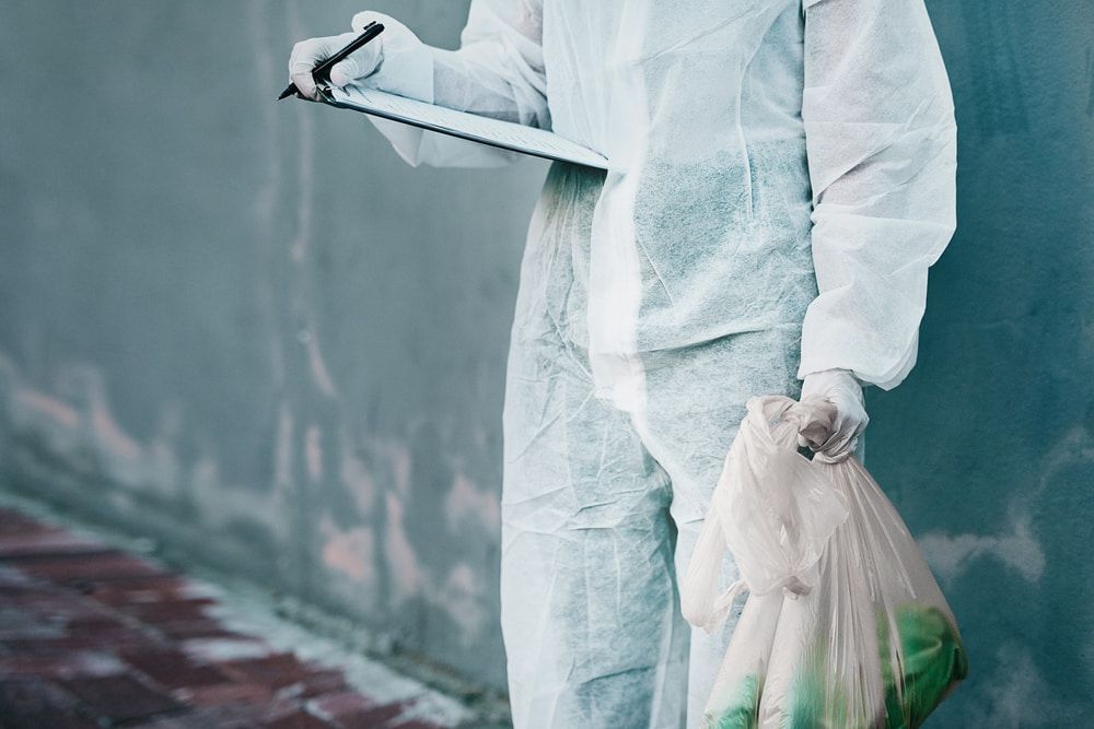 A Man in a Protective Suit is Holding a Clipboard and a Bag of Trash — Regina's Cleaning Group Pty Ltd In Lee Point, NT