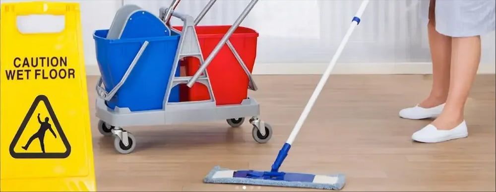A Person Mops a Wooden Floor Next to a Yellow Caution Wet Floor Sign