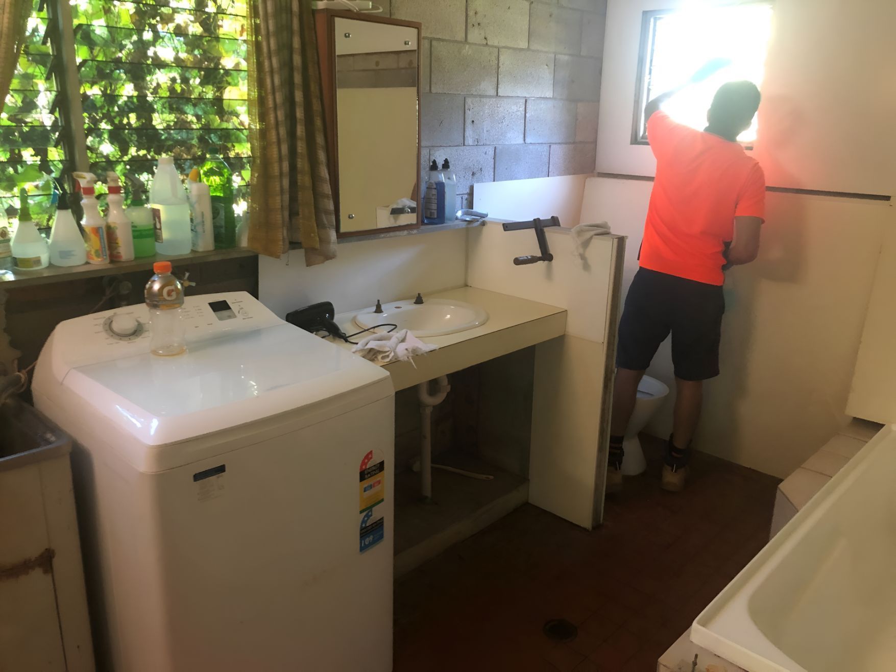 A Man In An Orange Shirt Is Measuring A Wall In A Bathroom — Regina's Cleaning Group Pty Ltd In Lee Point, NT