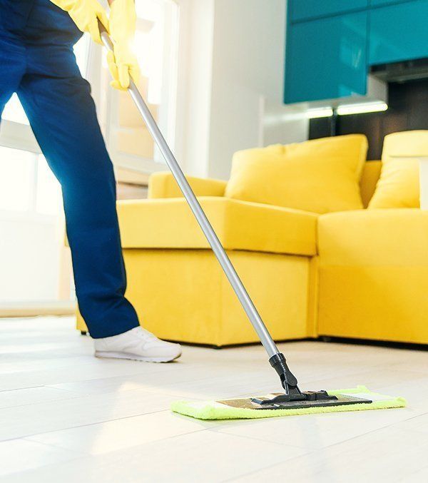 A Person Is Cleaning the Floor with A Mop in A Living Room — Regina's Cleaning Group Pty Ltd In Lee Point, NT