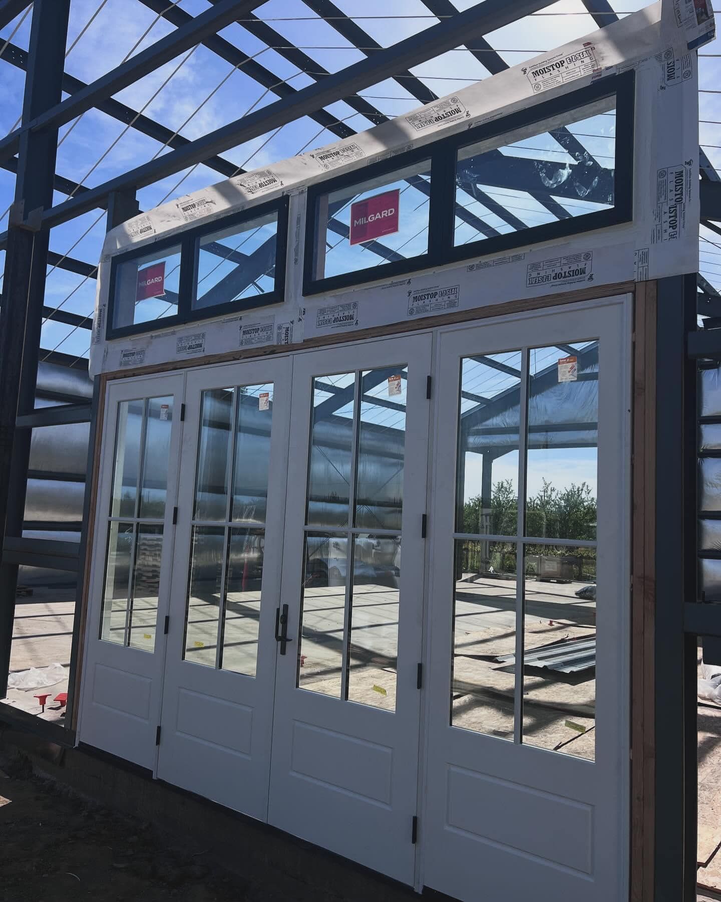 White French doors and transom windows installed in a metal-framed structure, construction site.