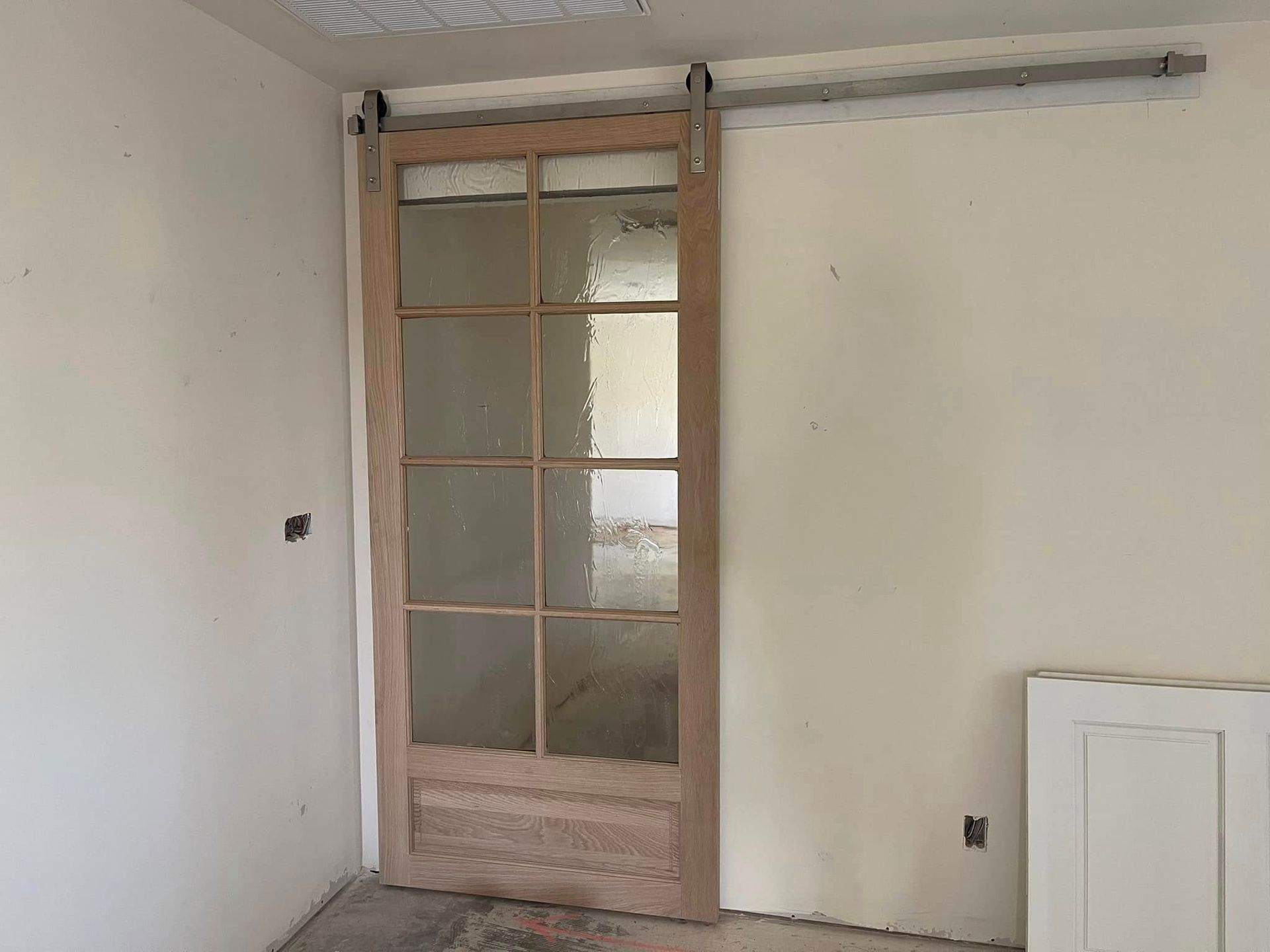 Barn door with glass panes on a track, against off-white walls in a room under construction.