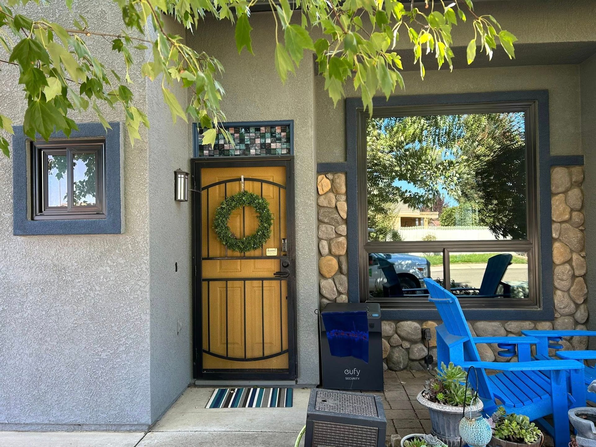 Tan door with wreath, beside a window and blue chairs on a patio.