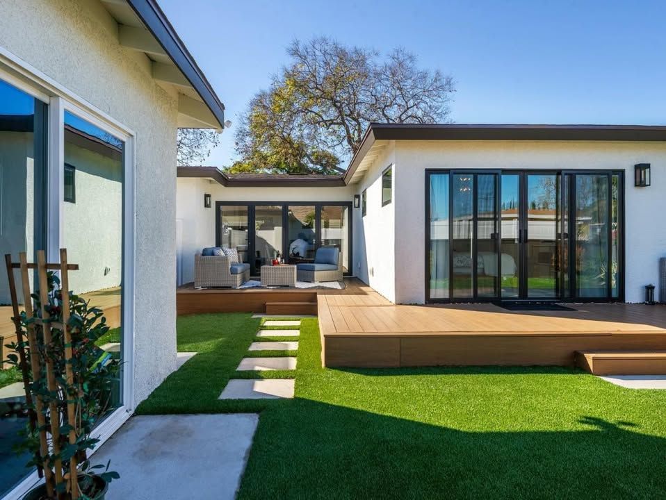 Backyard with a brown deck, green grass, and white houses with large black-framed doors.
