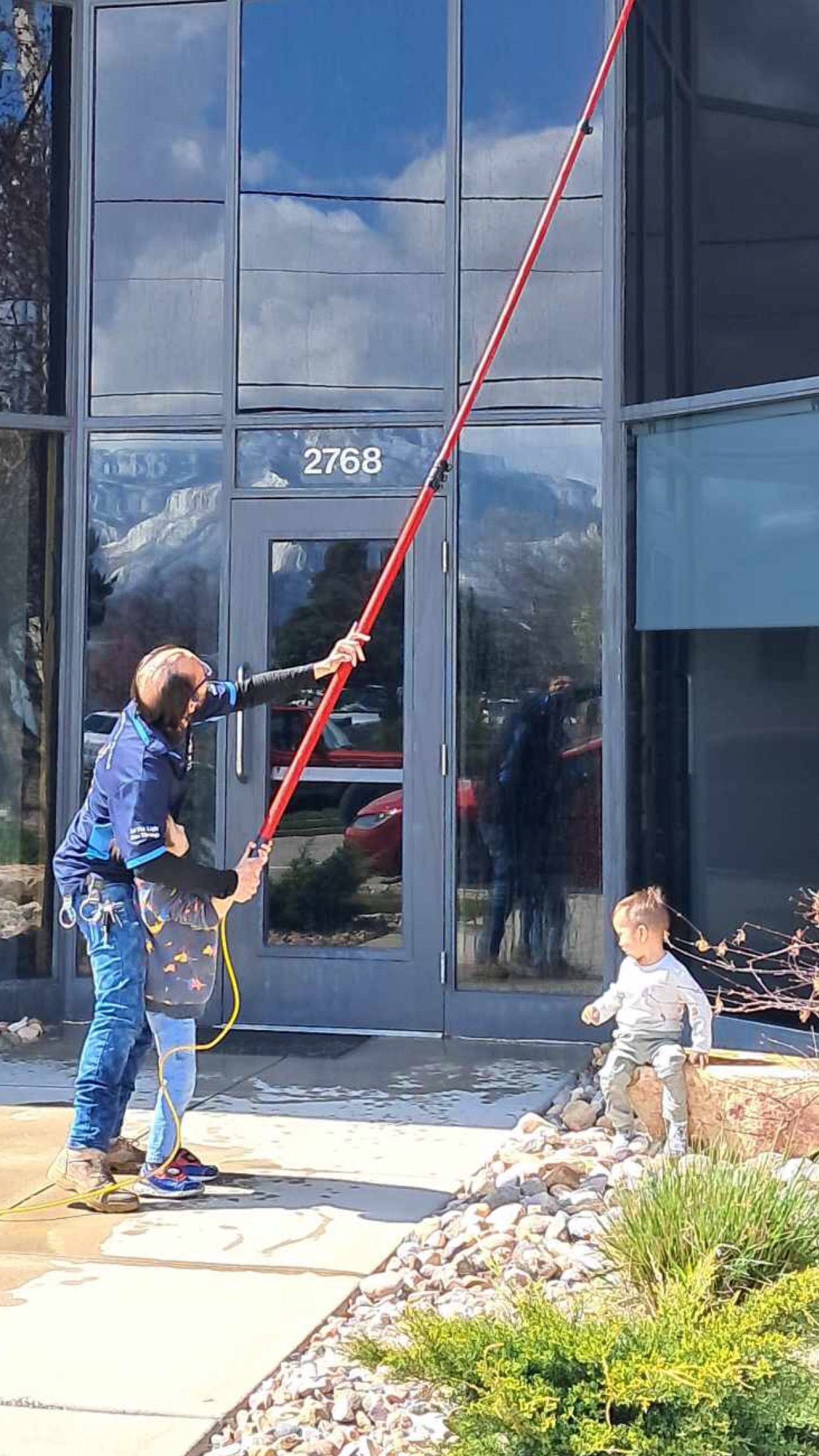 A man is cleaning the windows of a building with a long pole.