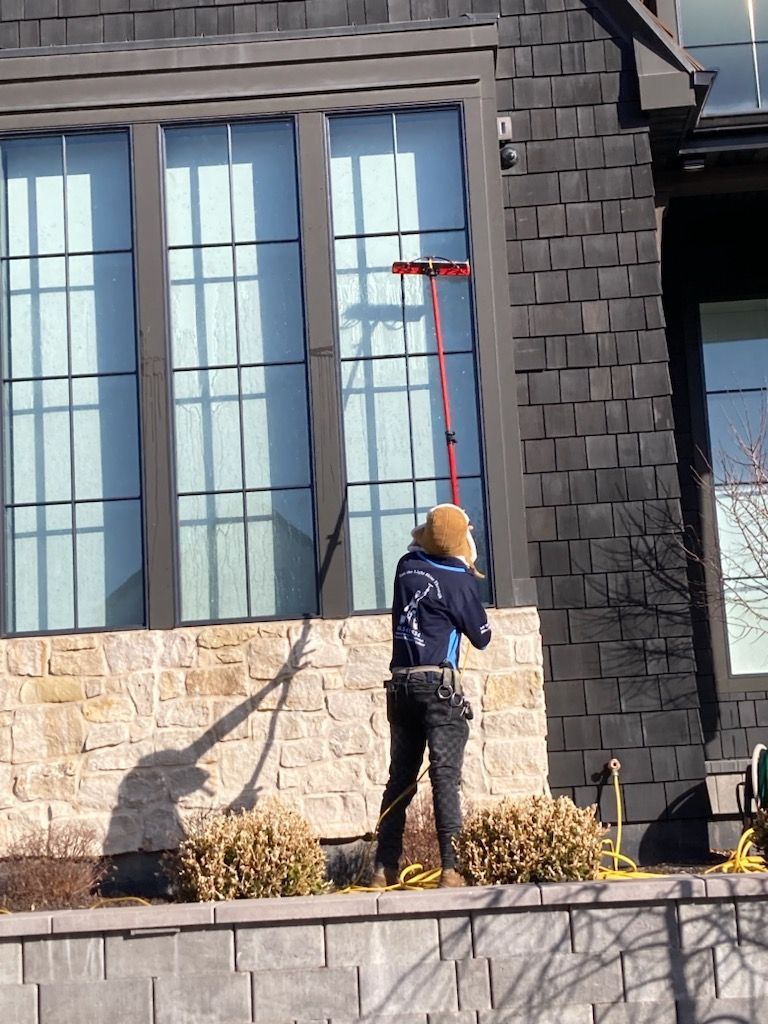 A man is cleaning the windows of a house with a long pole.