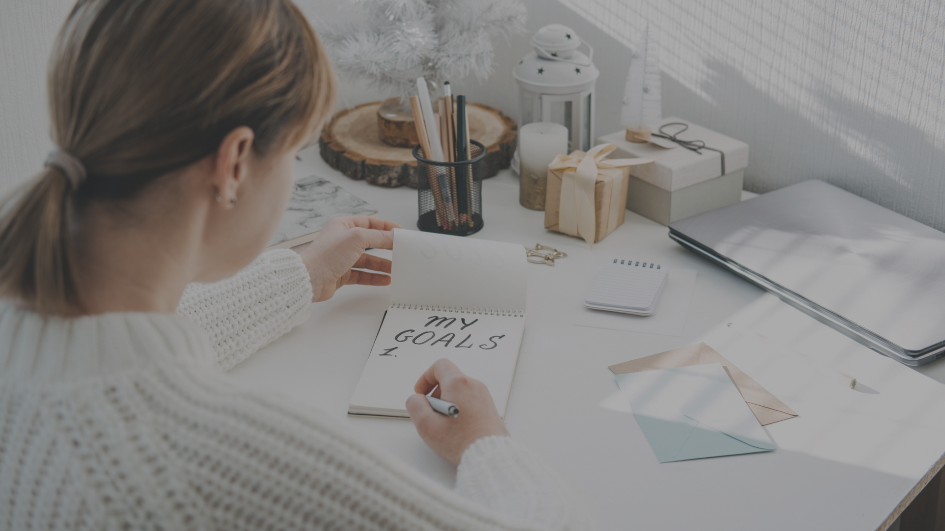 A woman sits at a neatly organized desk, writing 