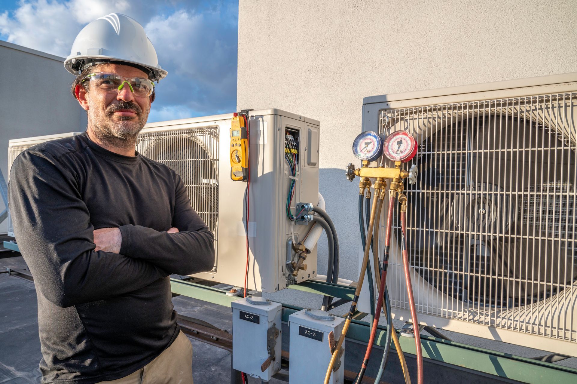 HVAC technician with crossed arms stands by rooftop air conditioning units, gauges visible.