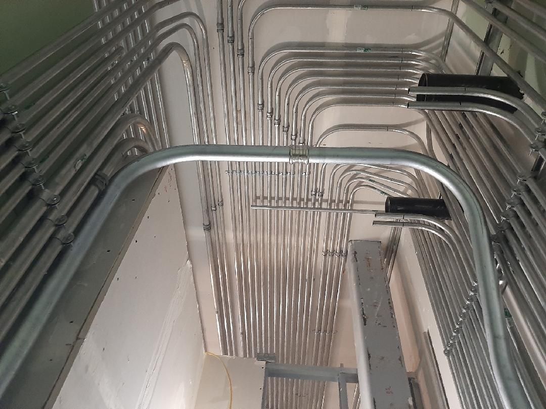 Metal electrical conduits, bent and arranged in a complex pattern on a ceiling.