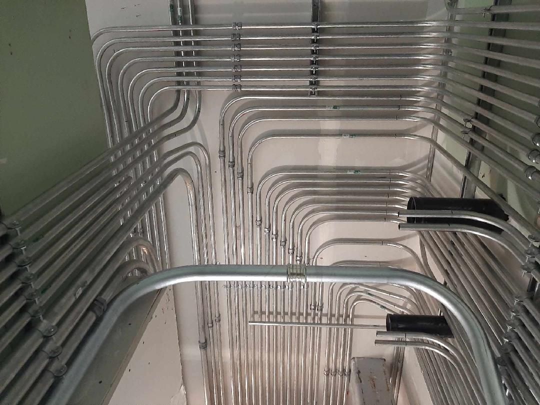 Silver electrical conduit pipes running along a ceiling, organized in rows and curves.