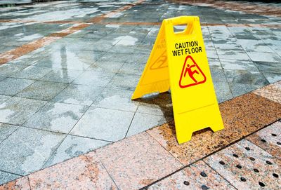 Yellow caution wet floor sign on a wet tiled sidewalk Yellow caution wet floor sign on a wet tiled sidewalk