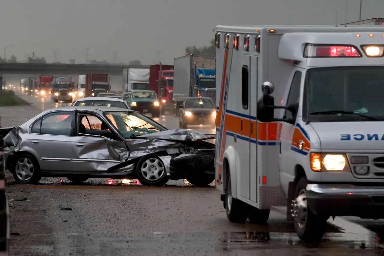 Wrecked silver car after a crash, with an ambulance