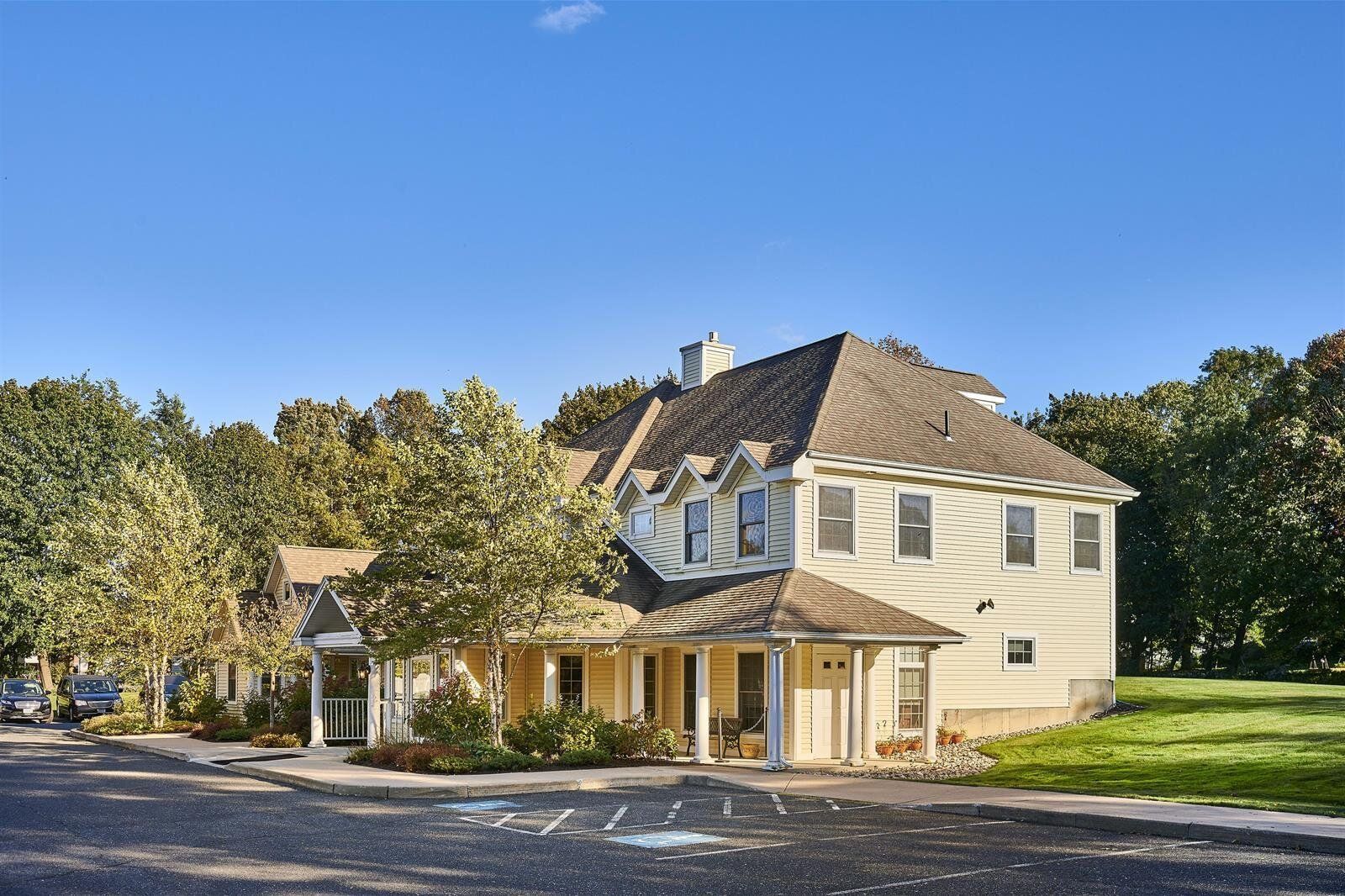 A large white house with a brown roof is surrounded by trees on a sunny day.