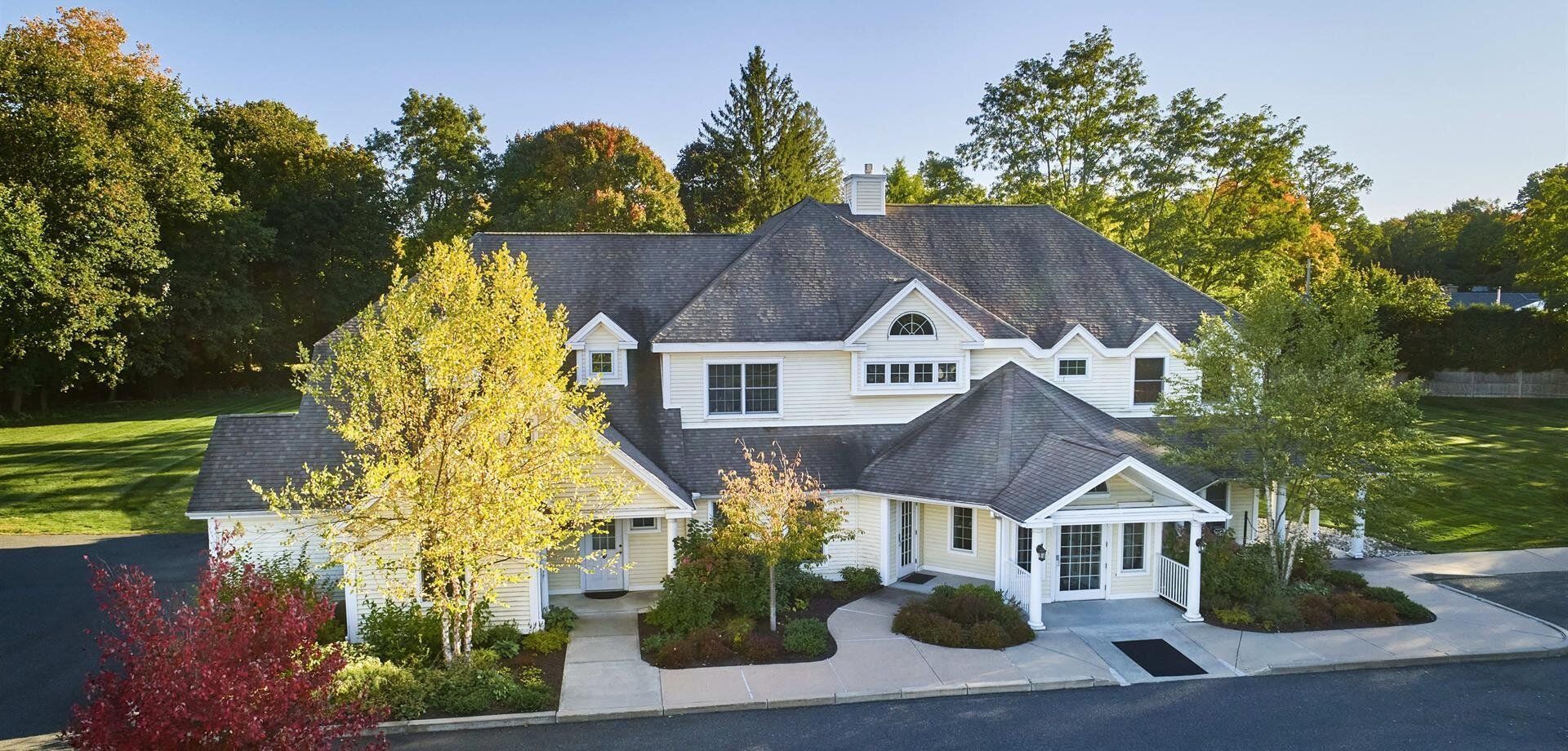 A large white house with a gray roof is surrounded by trees