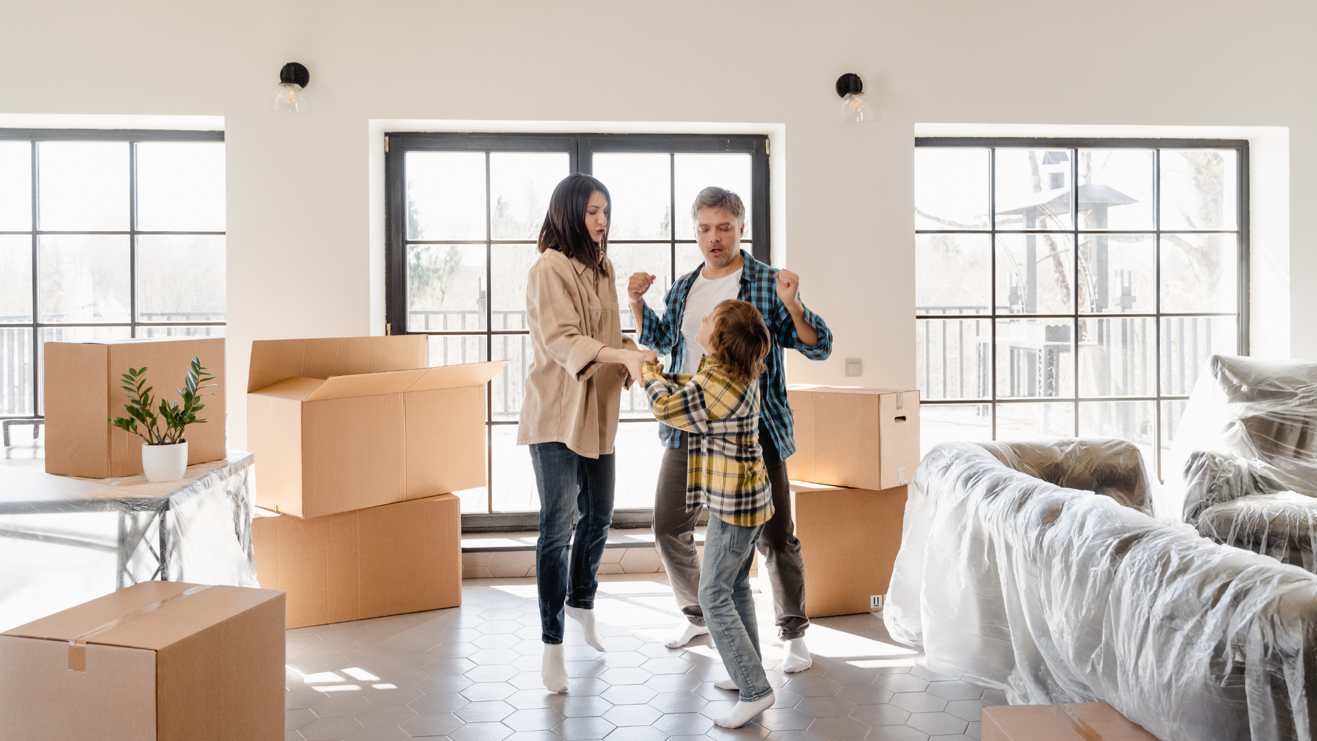 Family celebrates in new home surrounded by moving boxes, sunlight streams in windows.