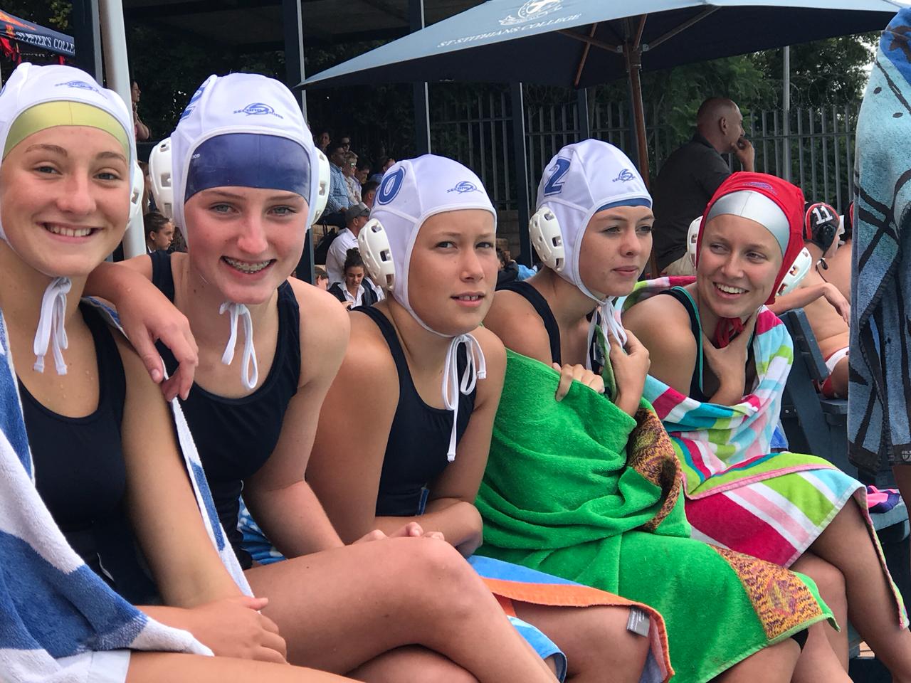 a group of young girls wearing swimming caps and towels are sitting next to each other .