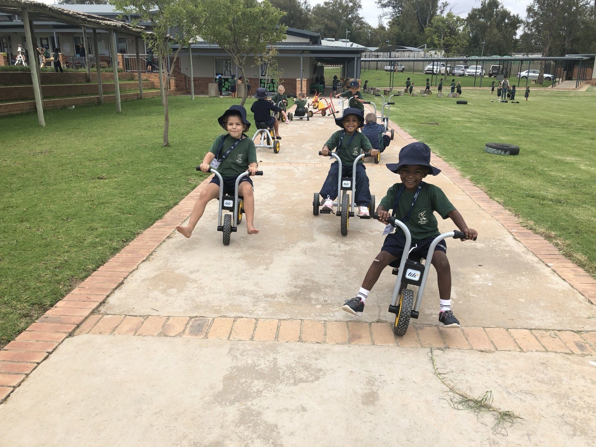 a group of children are riding tricycles down a sidewalk .