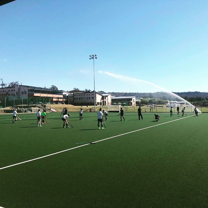 a group of people are playing field hockey on a field with a sprinkler spraying water .