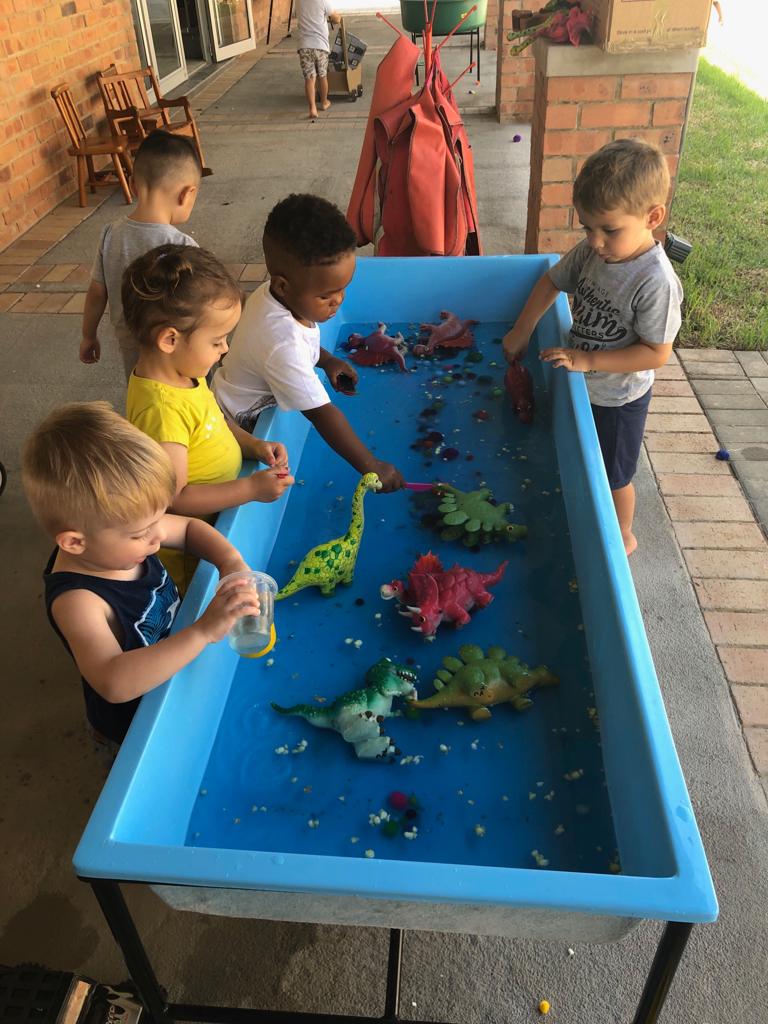 a group of children are playing with water and dinosaurs on a table .