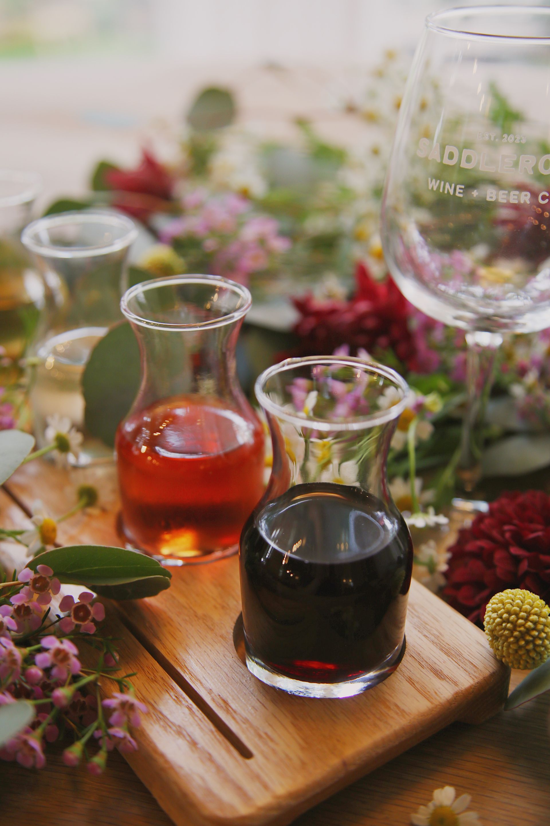 A wooden cutting board with three glasses of wine and flowers on it.