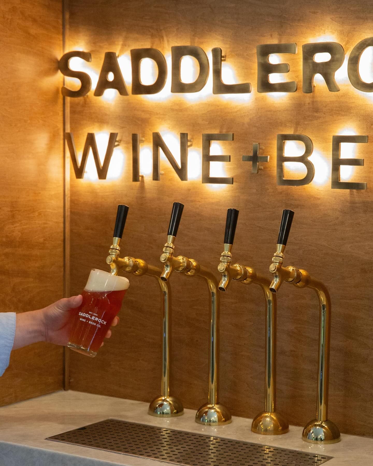 A person is pouring a glass of beer from a tap with a sign that says saddlerock wine + beer.