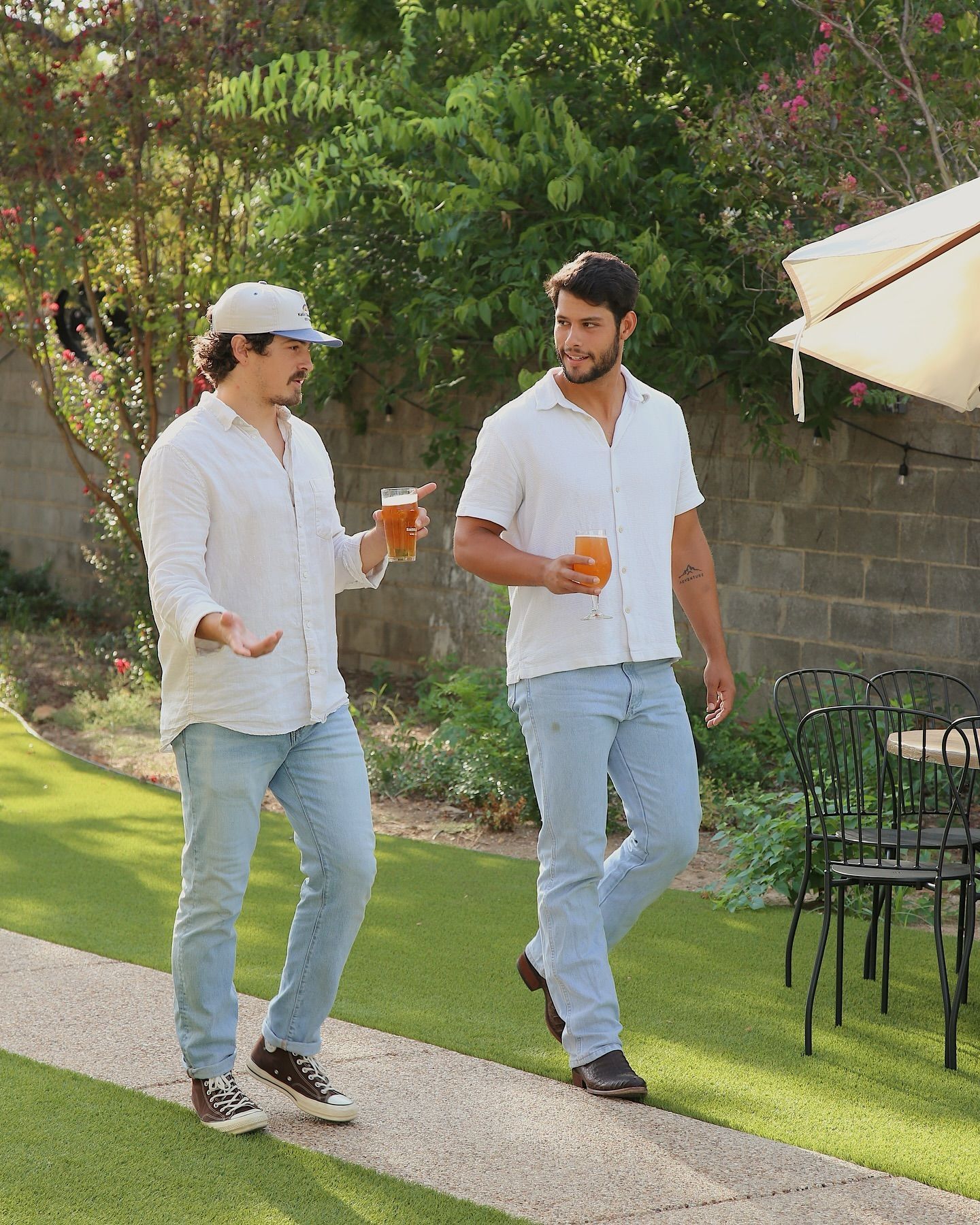 Two men are walking down a sidewalk holding beer glasses.