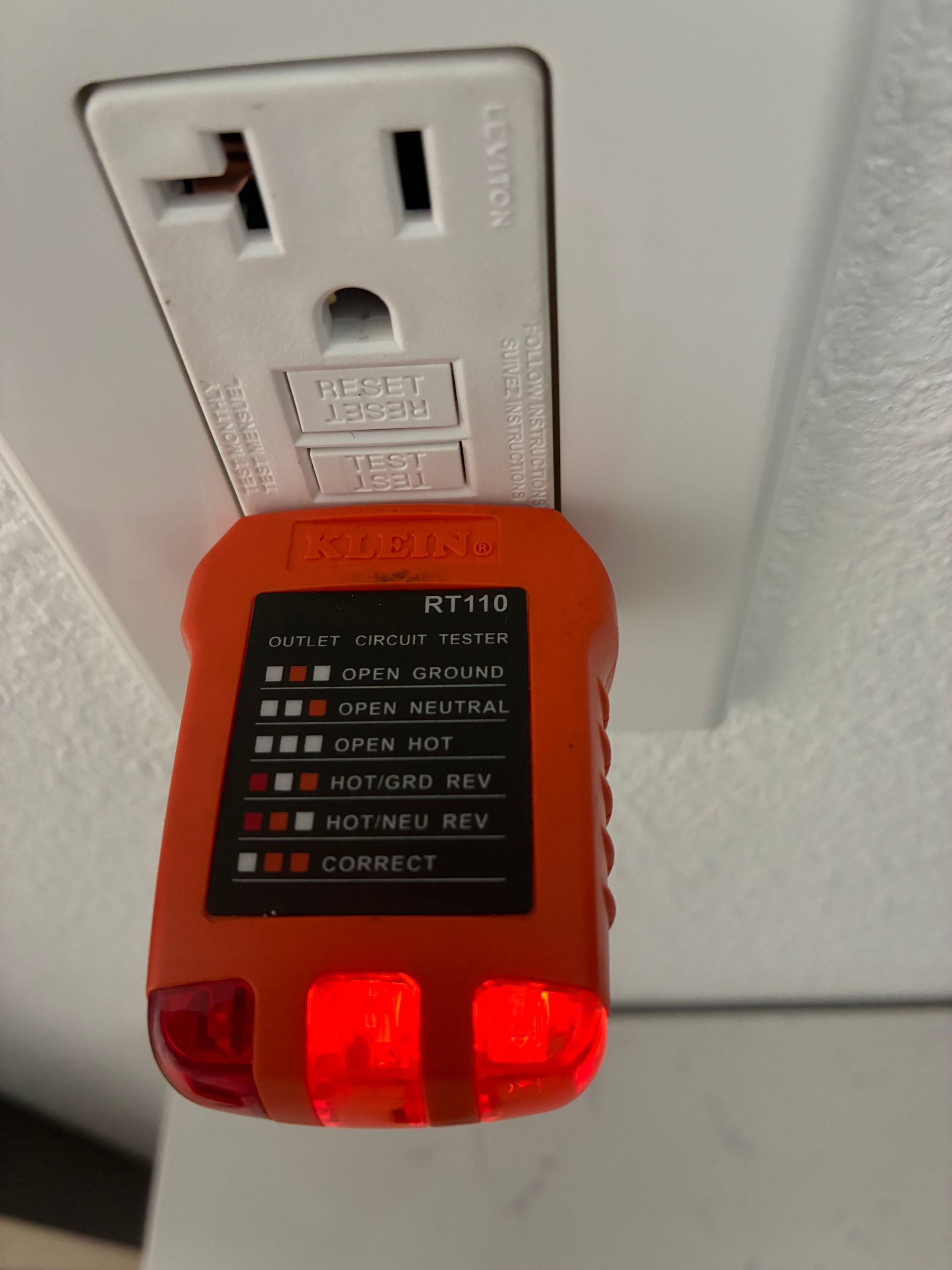 Orange electrical outlet tester plugged into a white outlet. The tester's red lights indicate a wiring problem.