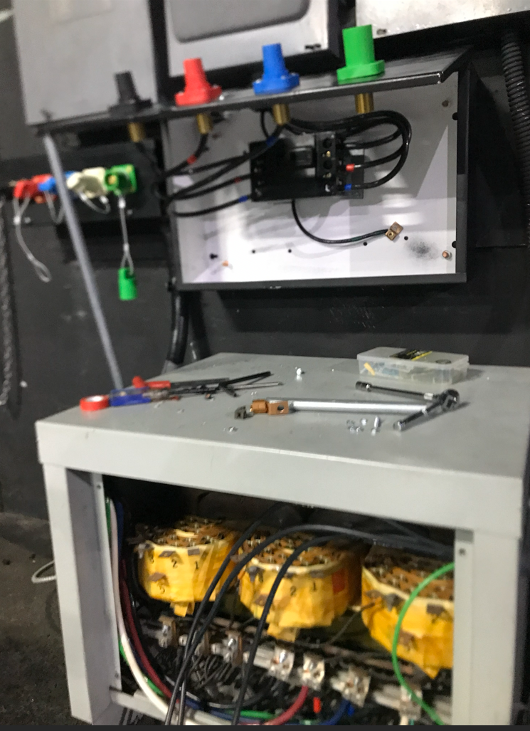 Electrical components inside a gray cabinet with yellow cylindrical containers. Colored lights sit above.