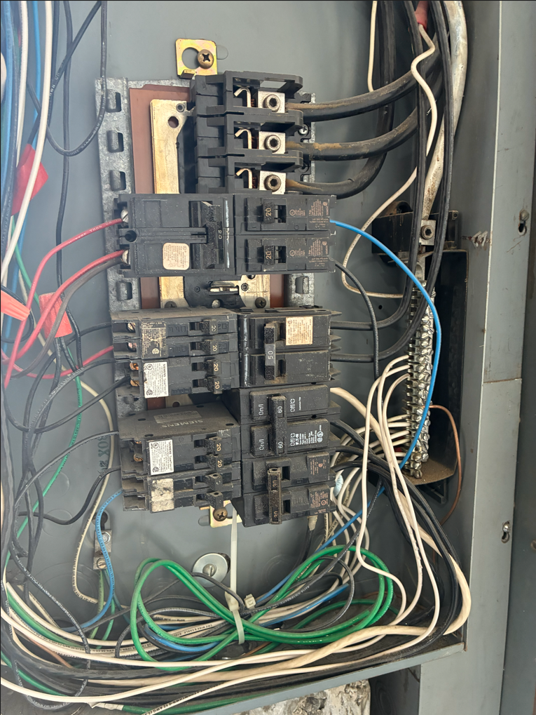 Open electrical panel with numerous circuit breakers and wires of various colors.