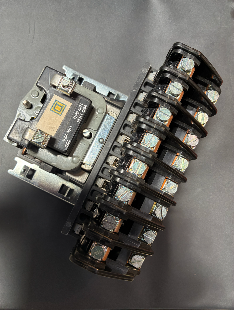 Electrical contactor with black plastic housing, silver terminals, and a small, beige component.