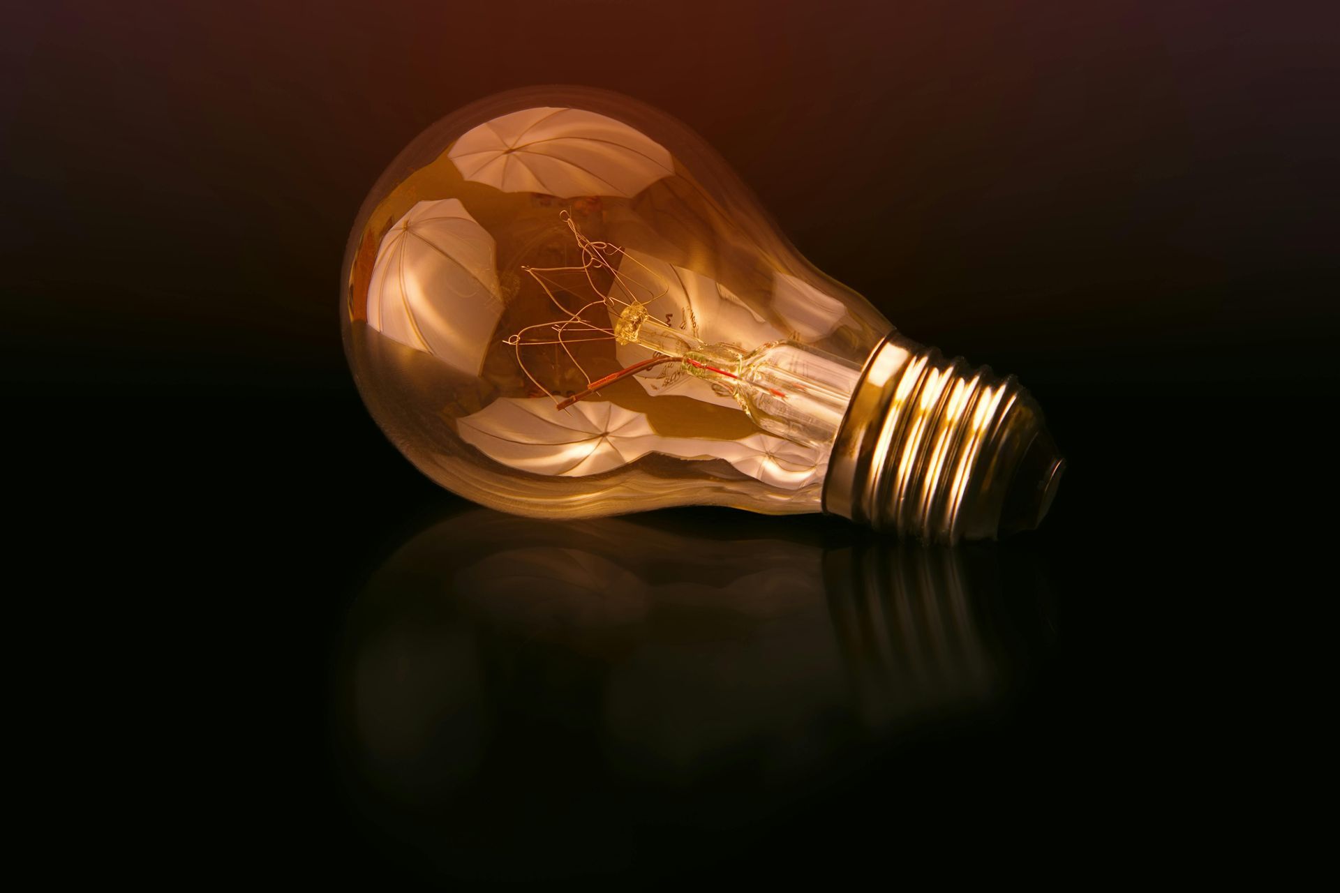 Lit light bulb on a reflective surface, glowing amber.