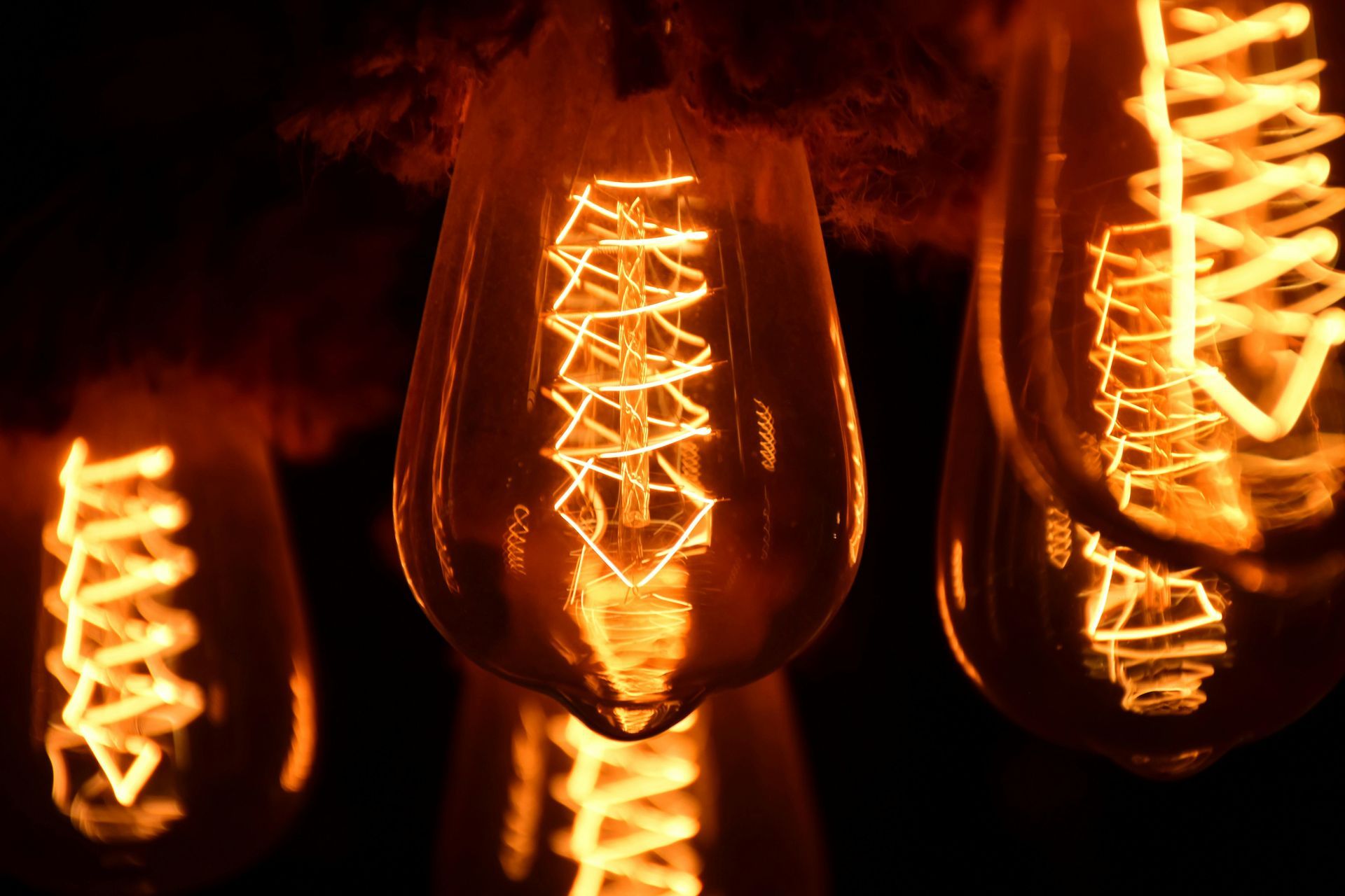 Close-up of lit, teardrop-shaped Edison light bulbs with glowing spiral filaments, dark background.