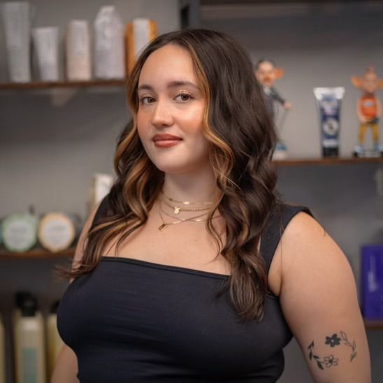 A woman with a tattoo on her arm is standing in front of a shelf full of hair products.