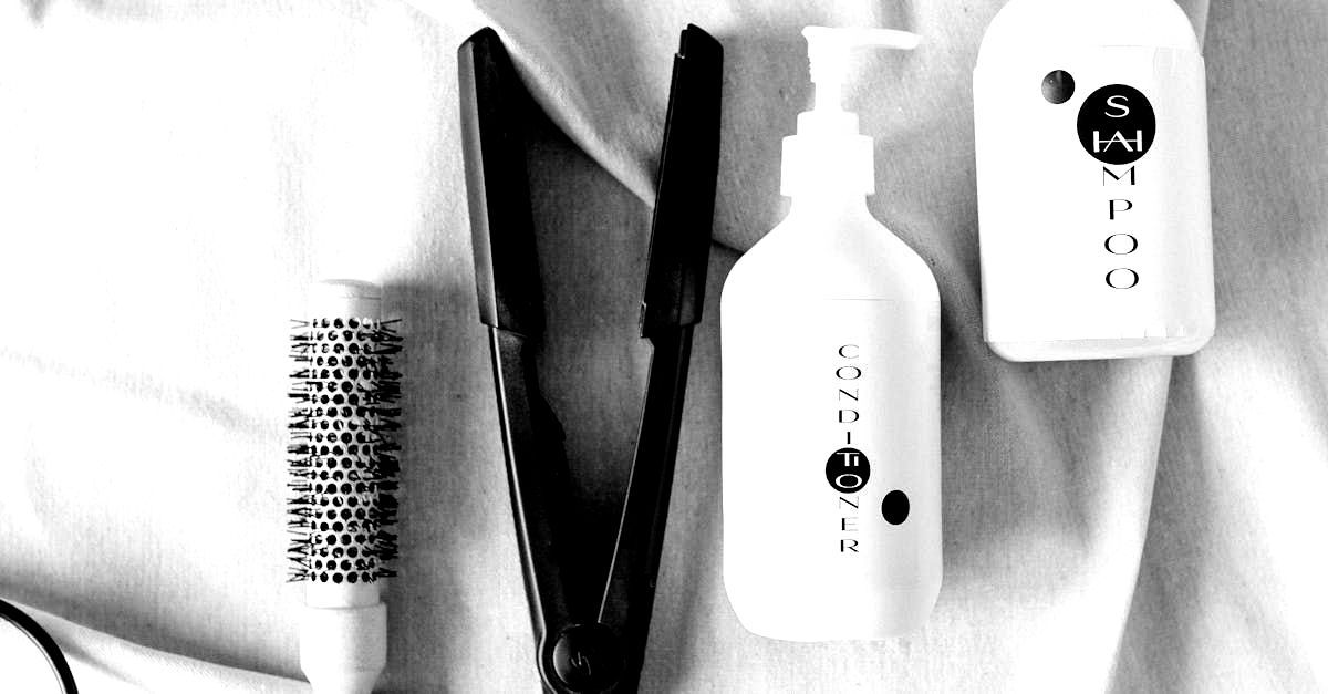 A black and white photo of a hair straightener a spray bottle and a brush