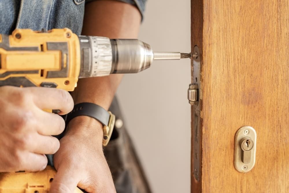 A Man is Using a Drill to Fix a Door Lock — A1 Maintenance and Building In Old Bar, NSW