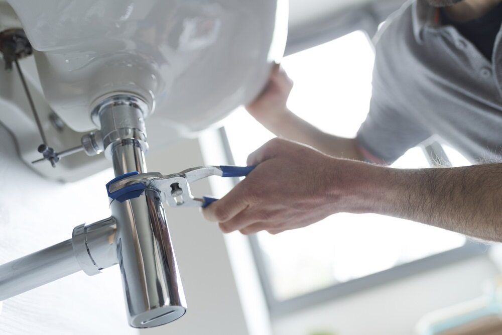A Man is Fixing a Sink With a Wrench — A1 Maintenance and Building In Old Bar, NSW