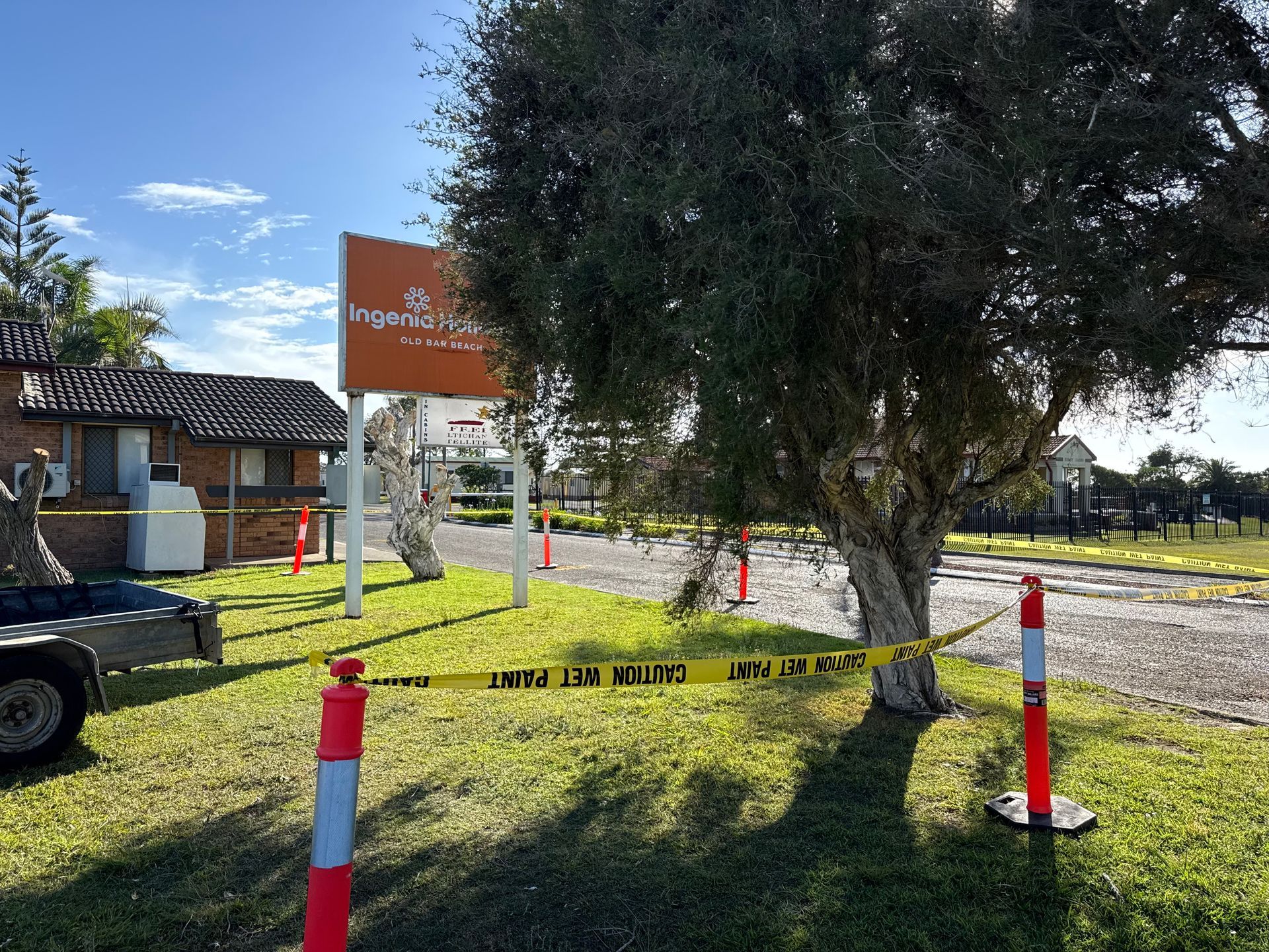 Exterior view of motel with caution tape. Sign, trees, brick buildings, and trailer visible under a sunny sky.  - A1 Maintenance and Building In Old Bar, NSW